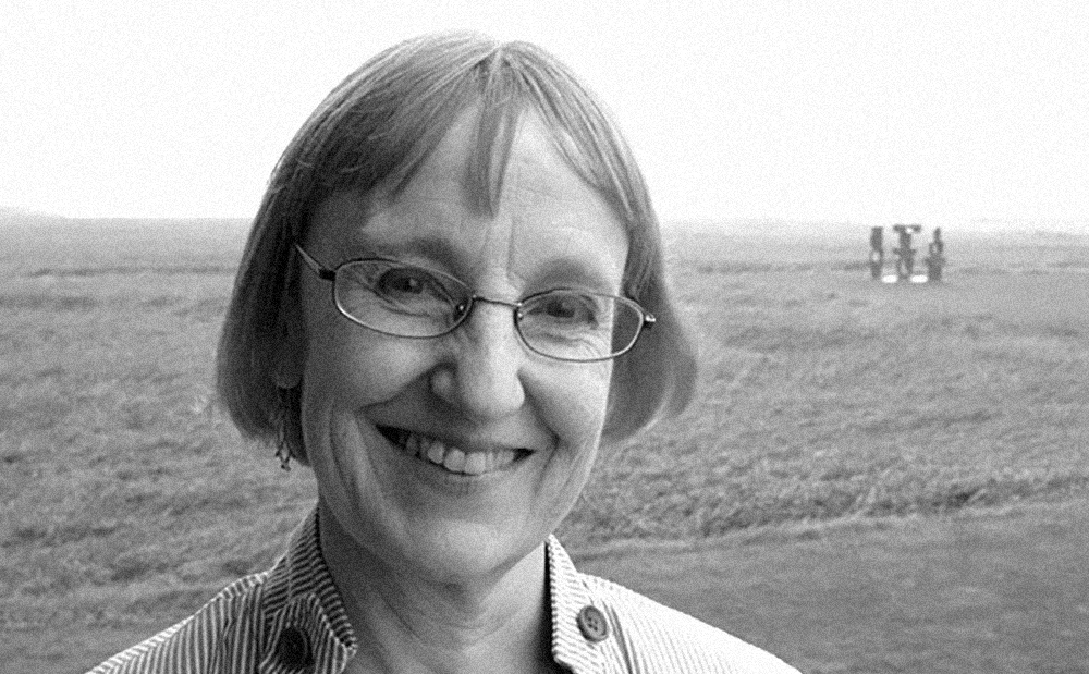 Black and white head and shoulders photo of Helena Nelson smiling into the camera against the background of a field
