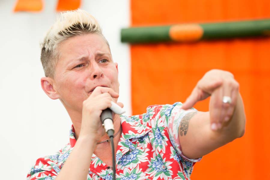 photo of Joelle Taylor with very short blonde hair in a flowery shirt speaking into a mic