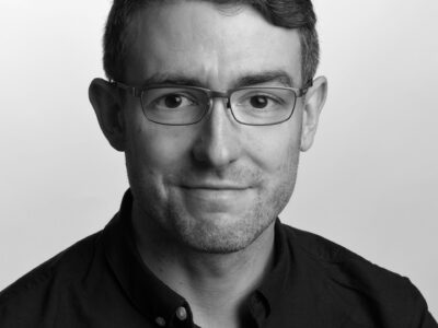 Black and white photo of Ben Wilkinson, a young friendly looking man with glasses