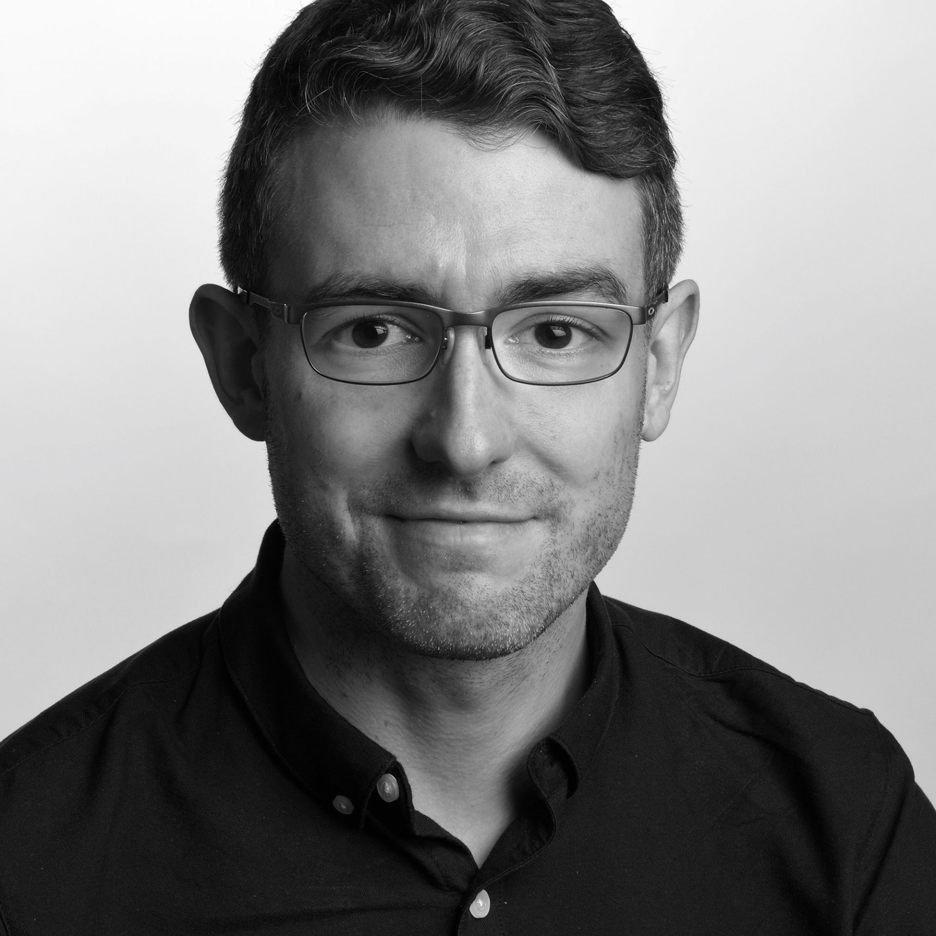 Black and white photo of Ben Wilkinson, a young friendly looking man with glasses