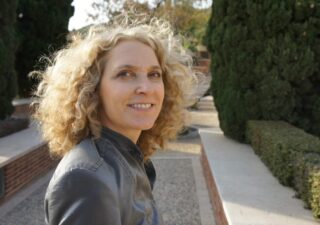 alice hiller with curly blonde hair wearing a grey jacket standing in a formal park