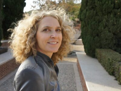 alice hiller with curly blonde hair wearing a grey jacket standing in a formal park