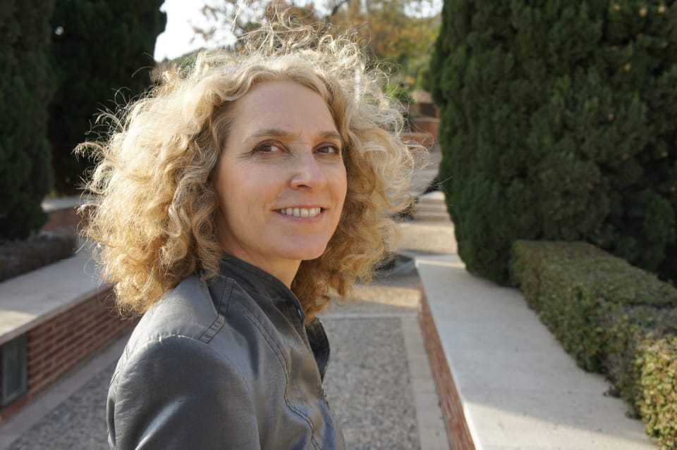 alice hiller with curly blonde hair wearing a grey jacket standing in a formal park