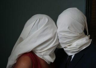 Editors Andy Brodie and Hilary Menos dressed up as 'The Lovers' by Magritte with white sheets over their heads, kissing