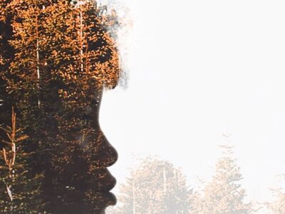Silhouette of a woman's face looking to the right of the image, her features are obscured be autumnal trees superimposed on the silhouette