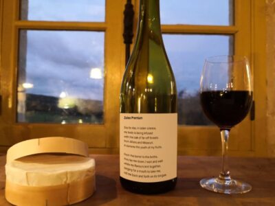 A ripe Camembert a bottle of Gaillac red wine with a poem on the label and a half full glass in front of a yellow window. The poem is Zaleo Premium by Matthew Stewart