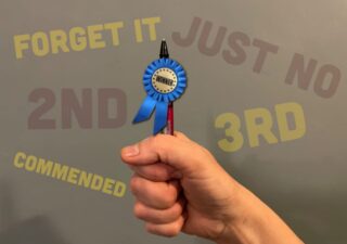 a hand holding a pen with a blue winners rosette attached to it
