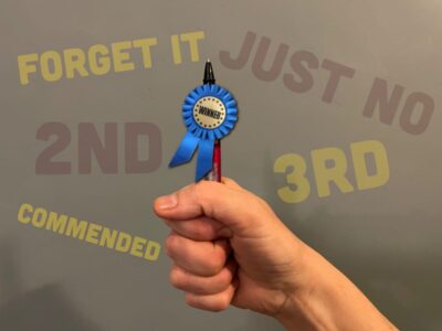 a hand holding a pen with a blue winners rosette attached to it