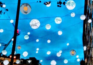 A dusk sky, lanterns are strung across the image, its all a bit blurred.