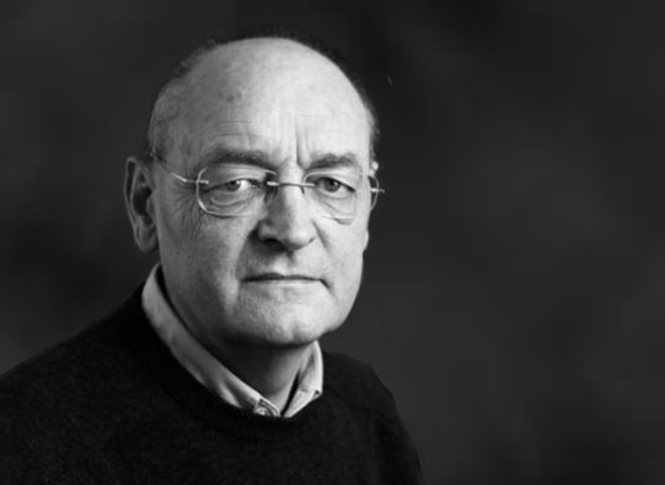 Black and white picture of William looking directly at the camera. He is balding and wearing glasses, he has a black sweater.