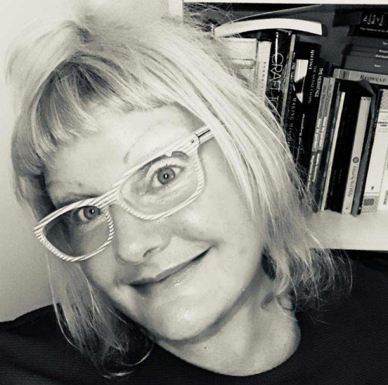 black and white portrait of Jane, head tilted, blond hair, glasses with white and grey striped frames, and a smile