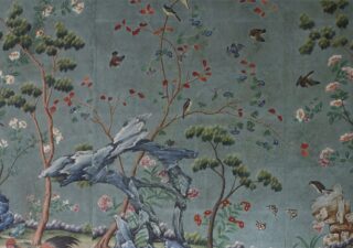 Blue Chinese wallpaper showing a watercolour design with trees and small birds. There are small flowers too.