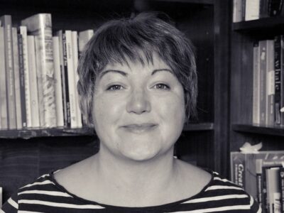 black and white picture of Wendy, she has short hair and a striped Breton style top. She has books behind .