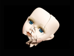 Black background with the face of a china doll, cracked, with piercing blue eyes.