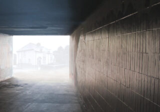 Looking through an underpass. A house can be discerned through distant mist.