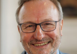 Close up of Mike Bartholomew-Biggs' smiling face. He has light coloured hair, a greying small beard and glasses.