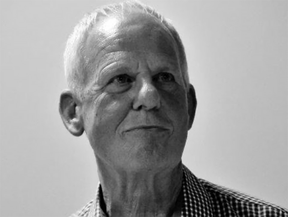 Black and white portrait photograph of Roger Elkin somehow looking both serious and impish.