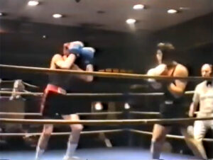 Grainy still from a colour film showing two boxers squaring up in a ring.