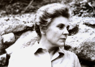 Black and white photo showing Elizabeth Bishop standing in front of some rocks.