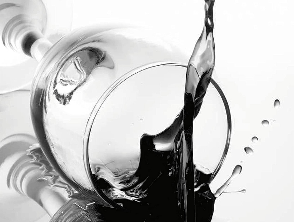 A close up black and white picture of a fallen wine glass, and dark liquid is splashing out.