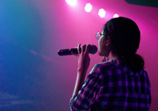 A woman holding a microphone. She is on stage with some funky purple and blue lighting.