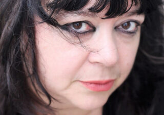 Close up photo of Diane Seuss' face. She looks intensely at the camera, heavy dark eyeshadow frames her eyes.