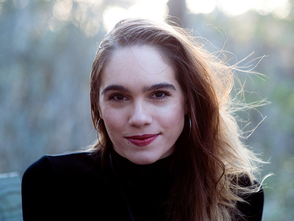 Photo of Leila Chatti looking at the camera. She has long brown hair and is wearing a black turtleneck sweater and red lipstick.