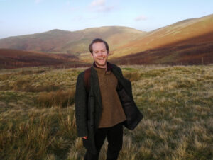 Stewart Sanderson standing in a field in front of the Cheviots. He is smiling.. well, why not? It looks like a great place.