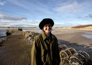 Photo of Katrina standing on the shore. Crab pots are behind her. Photo by Joe Grabham.