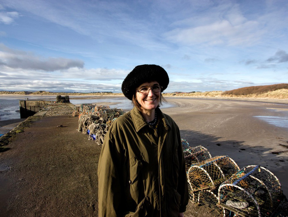 Photo of Katrina standing on the shore. Crab pots are behind her. Photo by Joe Grabham.