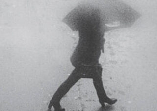 Blurred black and white photograph of a woman walking with an umbrella.