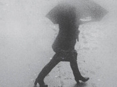 Blurred black and white photograph of a woman walking with an umbrella.