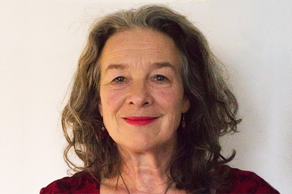Photo of Jackie Wills. She has long brown hair with flecks of grey, and red lipstick.