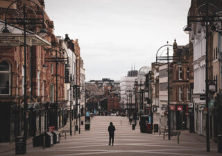 Photograph showing a streets in Leeds city center. They are empty apart from one figure in the middle of the street