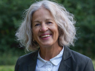 Photo of Vanessa Lampert. She is wearing a blue jacket and smiling. She has shoulder length grey hair.