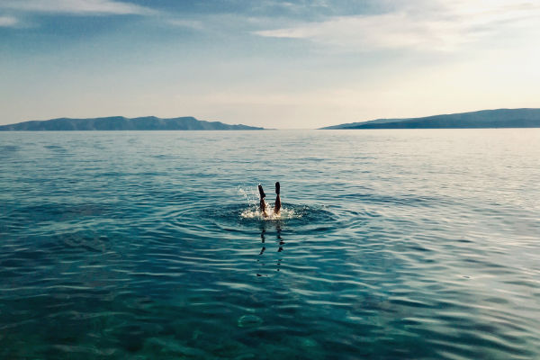 A photograph of someone diving into the sea. We can only see the legs.