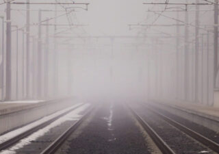 A misty photo showing train tracks disappearing to a vanishing point.