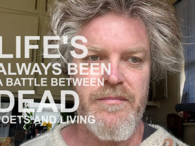 A photograph of a bearded man with wild greying hair. The words 'LIFE'S ALWAYS BEEN A BATTLE BETWEEN DEAD POETS AND LIVING' are superimposed in white text.