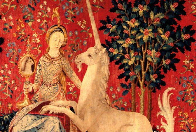 Section of what looks like a red tapestry showing a woman a unicorn and a fruit tree. the woman is sitting and the unicorn is resting its front hooves on the woman's leg. The tree remains impassive.