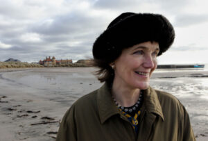 Photograph of Katrina walking on a beach wearing a round black hat. (photo Joe Grabham).