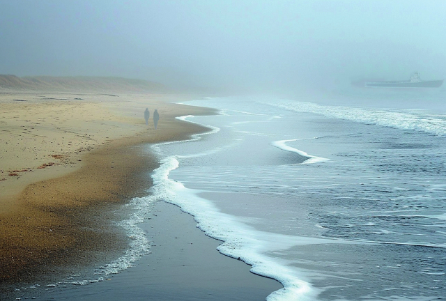 Photograph of two people walking on the beach at low tide. A shadowy coaster is seen in the background. This may or may not be relevant.