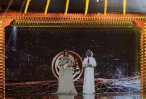 A fancy proscenium arch on a stage in gold and red. Underneath on the stage are a man and a woman in Arabic dress.