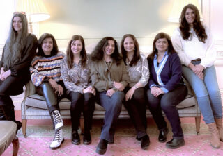 Seven women sitting on a sofa.